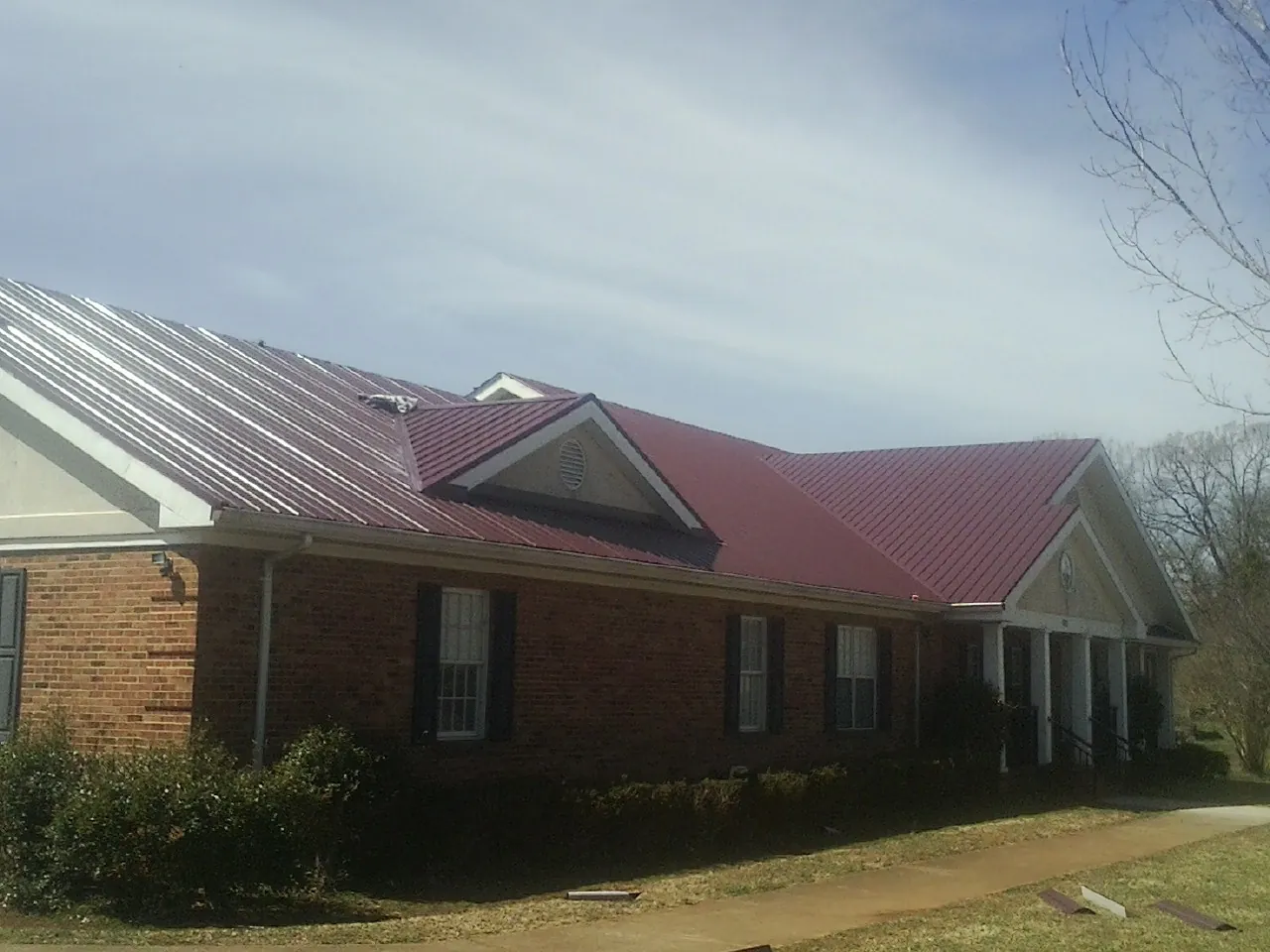 Red metal roof with gabled entries on a long brick building, from a Hail Damage Roof Repair job in Franklin Park